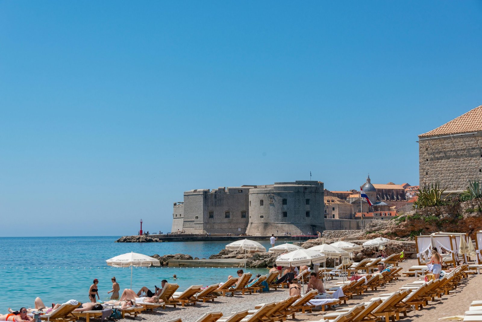 Charming sandy beach and sunny day by Dubrovnik's historic fort with loungers and umbrellas.