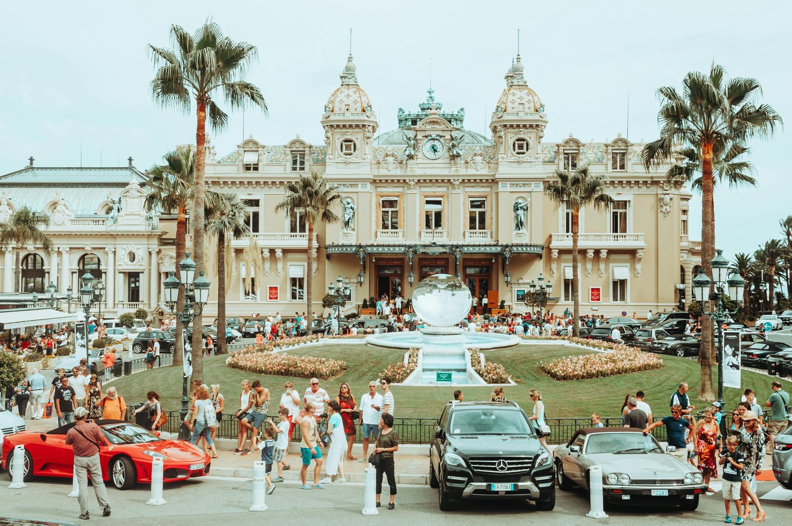 Monte Carlo Casino facade with luxury cars and palm trees in the foreground.